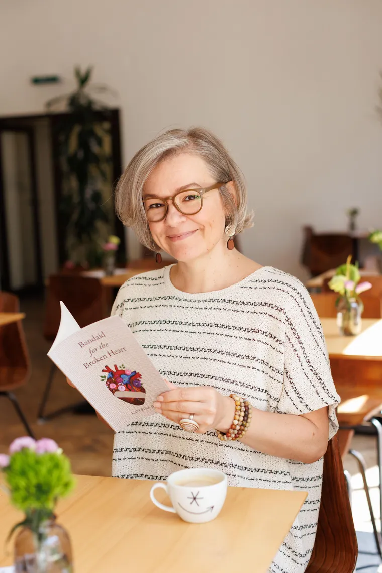 Katerina Szép smiling at a café table, holding a copy of one of her poetry collections